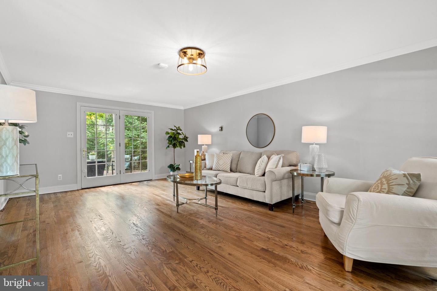 Staged living room with hardwood floors, a beige sofa, and French doors opening to greenery.