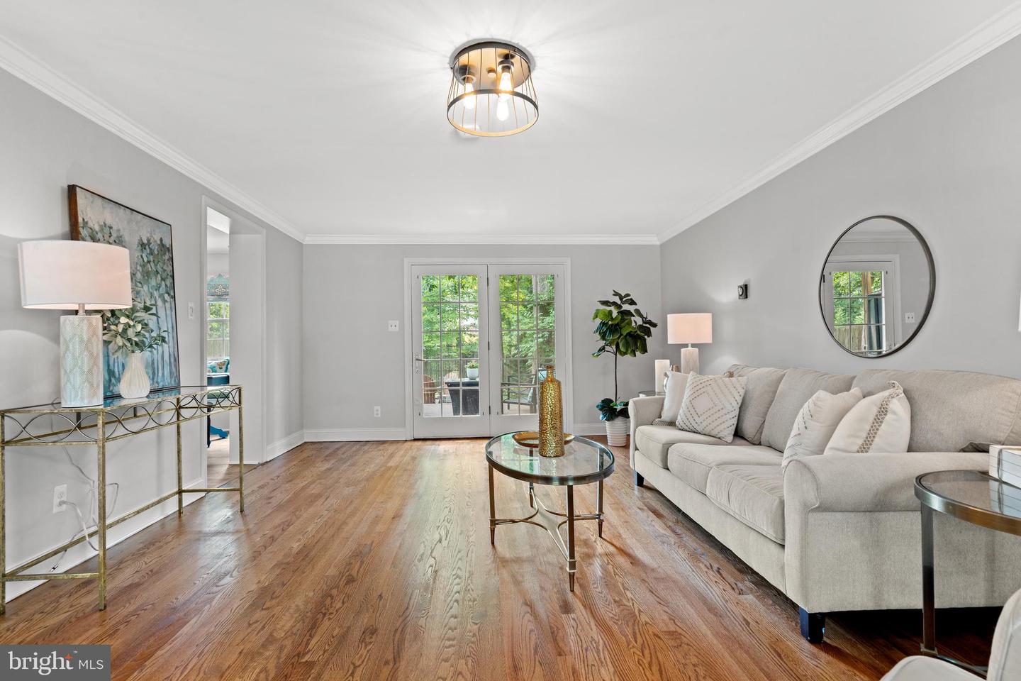 Living room with a light sectional, hardwood floors, and French doors opening to greenery.