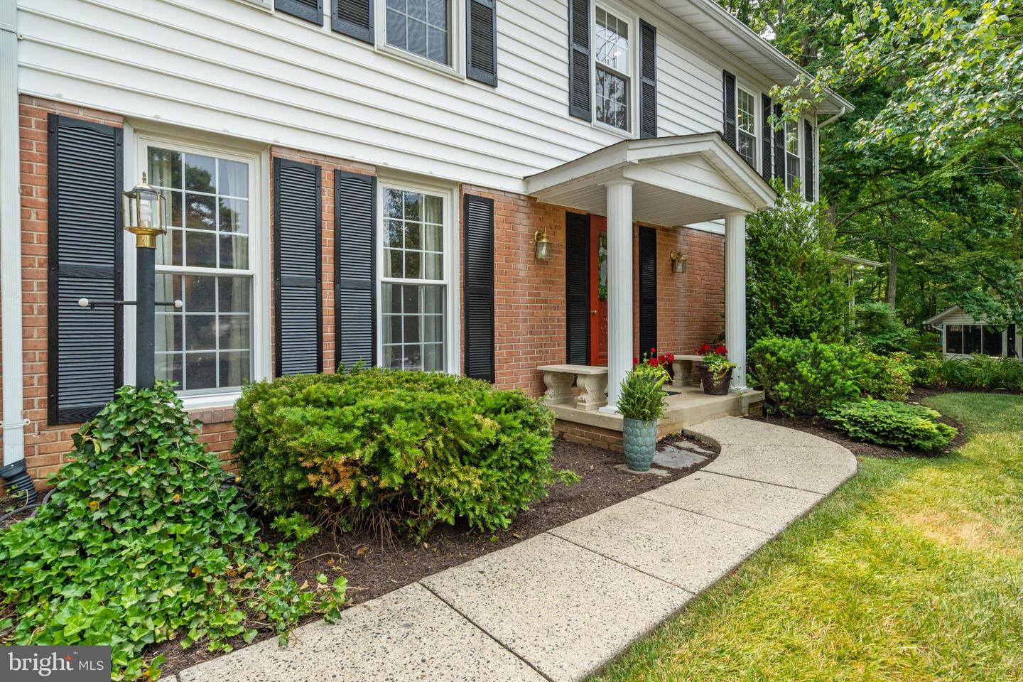 Two-story brick and white-sided home with black shutters, a columned porch, and a curved walkway.