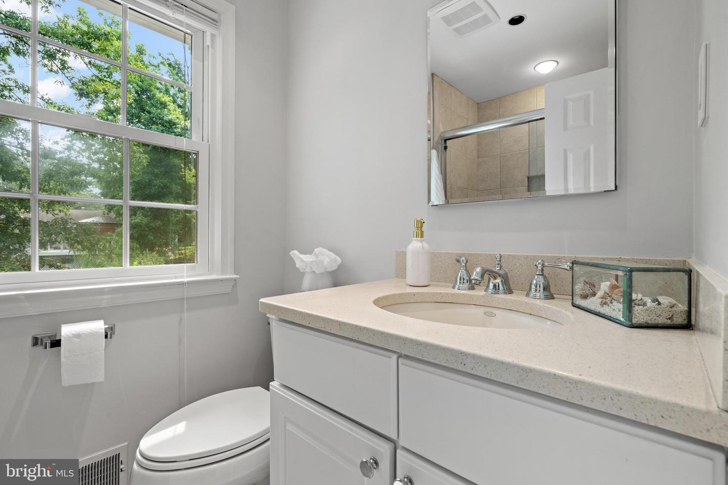 Bathroom with a white vanity and large window overlooking leafy trees.