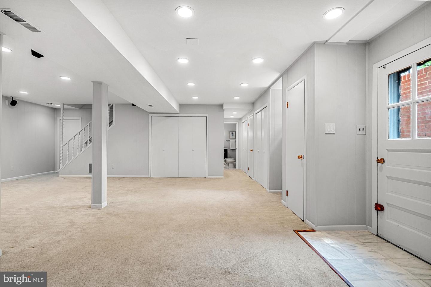 Vacant carpeted basement rec room with a staircase, paneled walls, and a tiled entry.