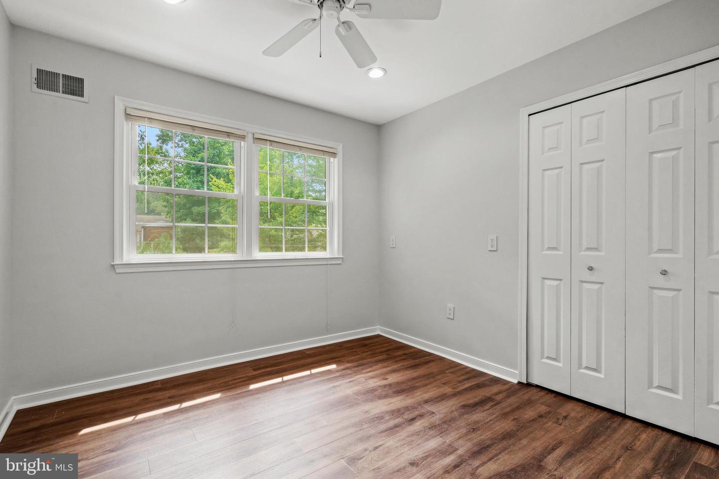 Vacant bedroom with wood-look flooring, two sunny windows, a ceiling fan, and a wide closet.