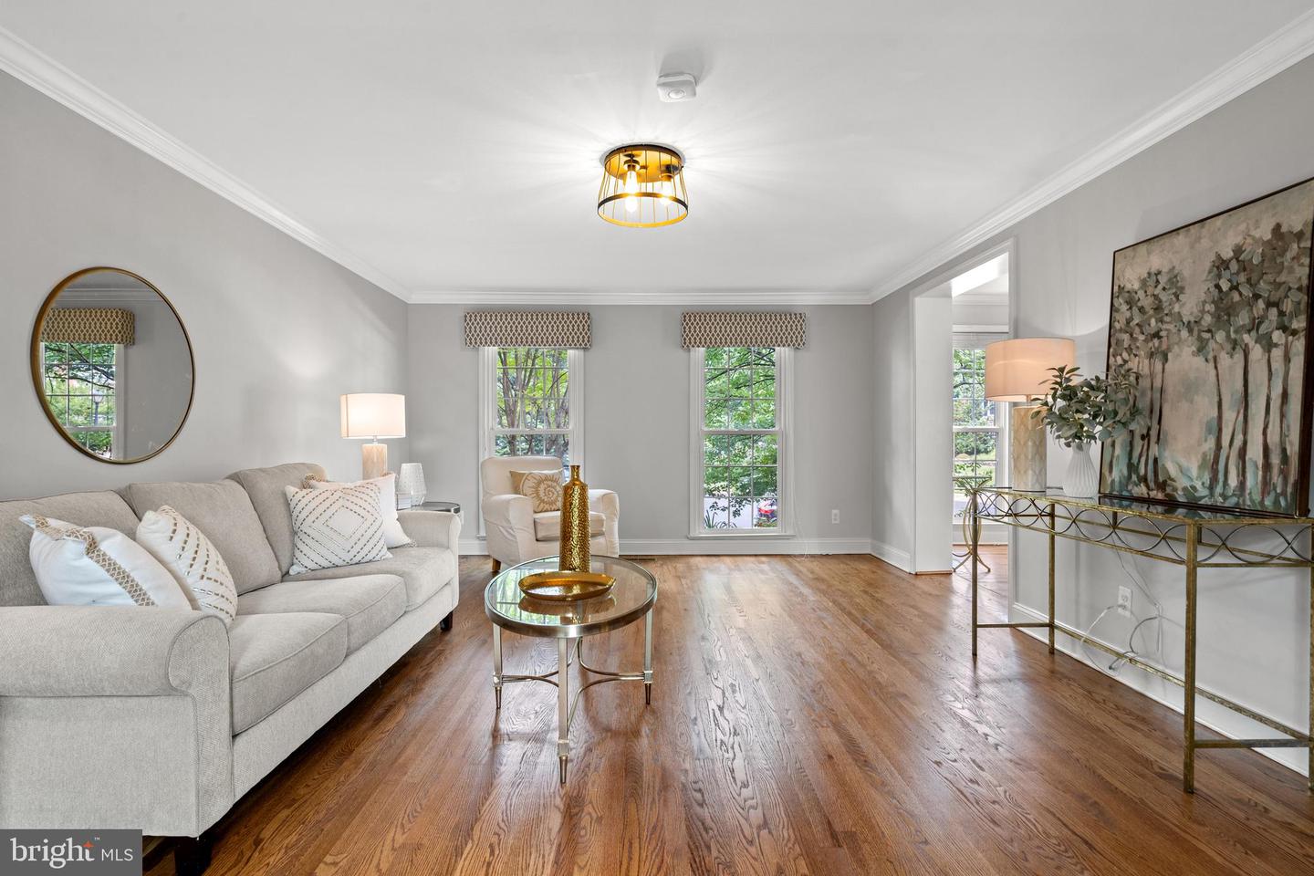 Staged living room with a light sofa, hardwood floors, and tall windows.