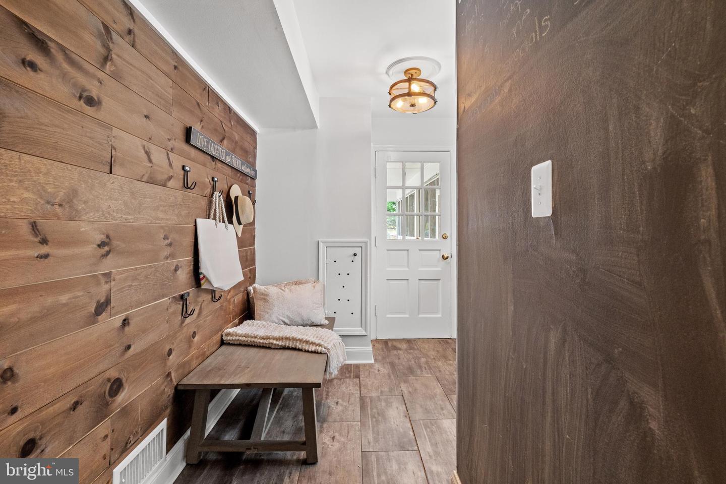 Entryway with a cushioned bench, wood-plank wall with hooks, and white glass-paneled door.