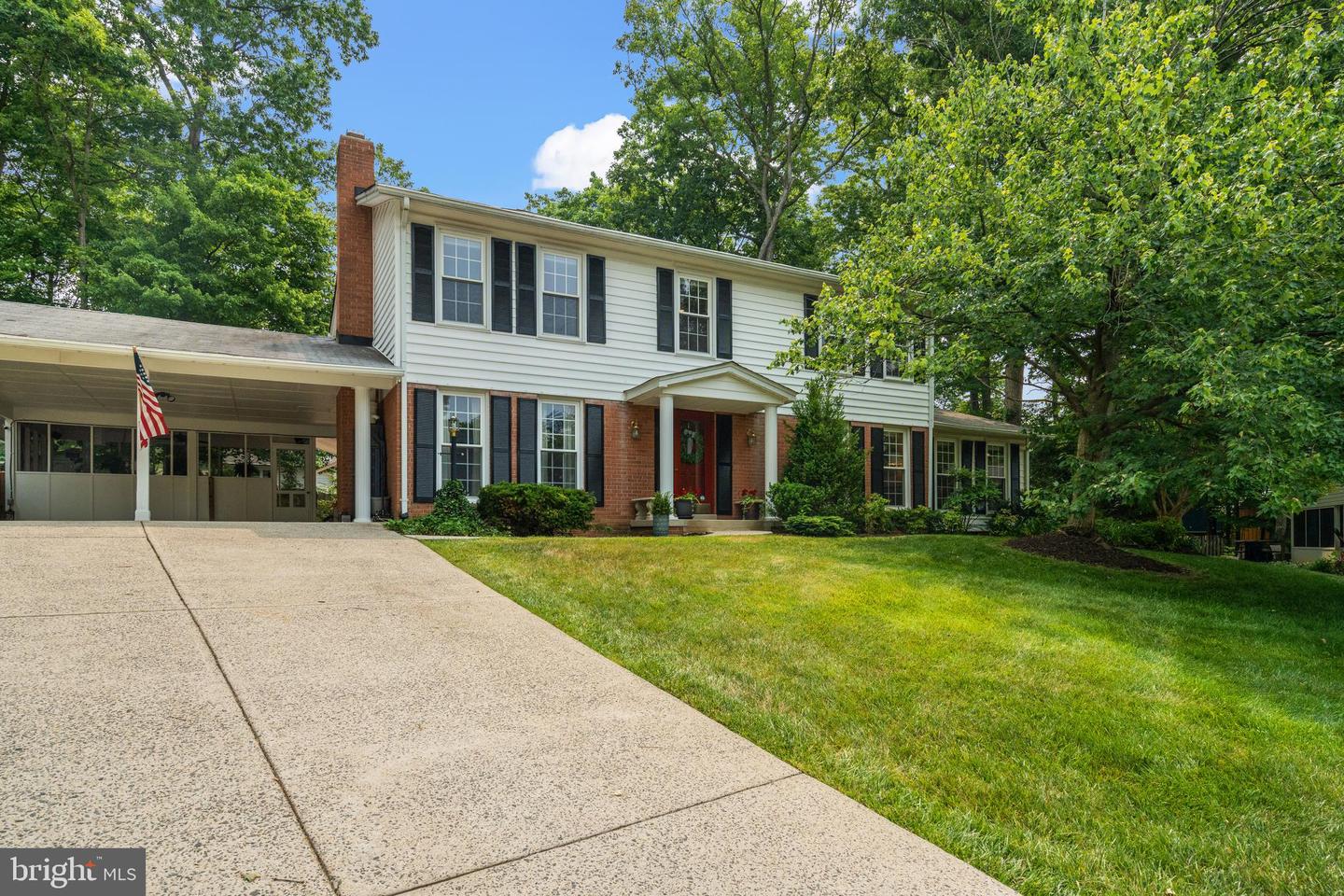 Two-story brick and white-sided house with black shutters, a red front door, and a broad driveway.