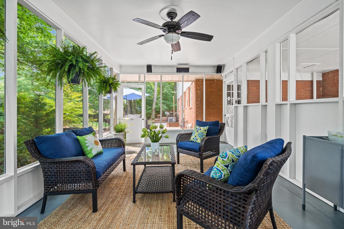 Enclosed sunroom with wicker seating, blue cushions, large windows, and leafy views.