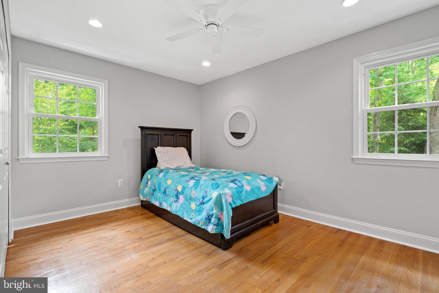 Bedroom with a turquoise quilt on a dark wood bed, hardwood floors, and two tree-facing windows.
