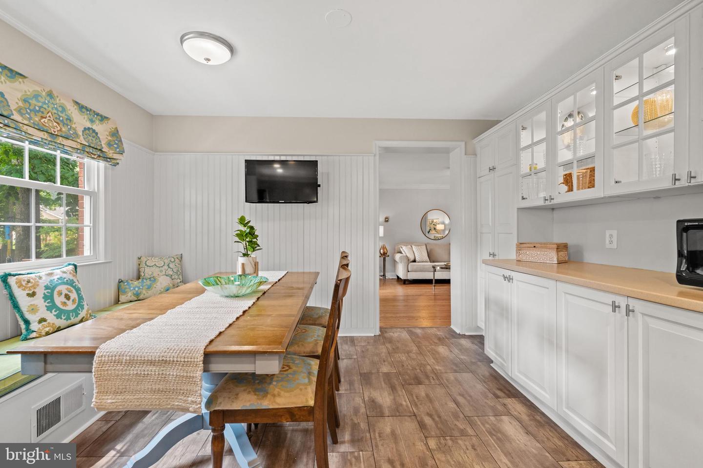 Dining area with a wooden table, patterned window seat, and white built-in cabinetry.