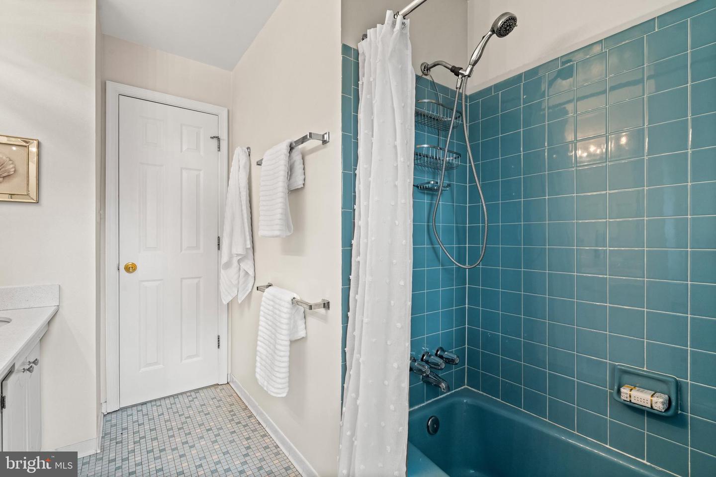 Bathroom with a teal tiled tub and shower, chrome fixtures, and white towels.
