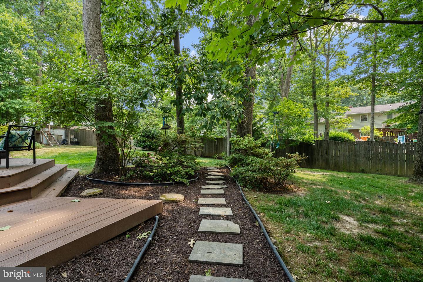 Wooded backyard with a raised deck and stepping-stone path through landscaped beds.