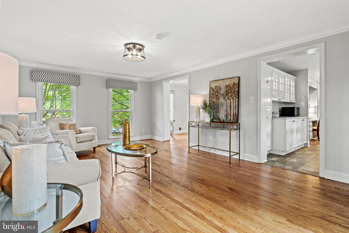 Living room with hardwood floors, bright windows, and an open view into the kitchen.