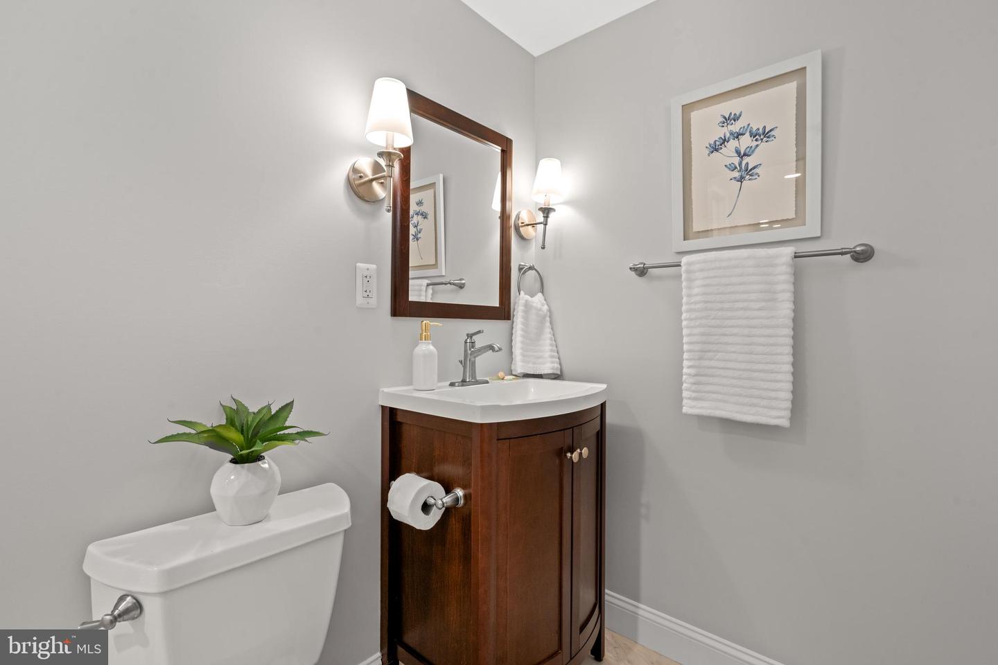 Bathroom vanity with a dark wood cabinet, white sink, botanical print, and folded towels.