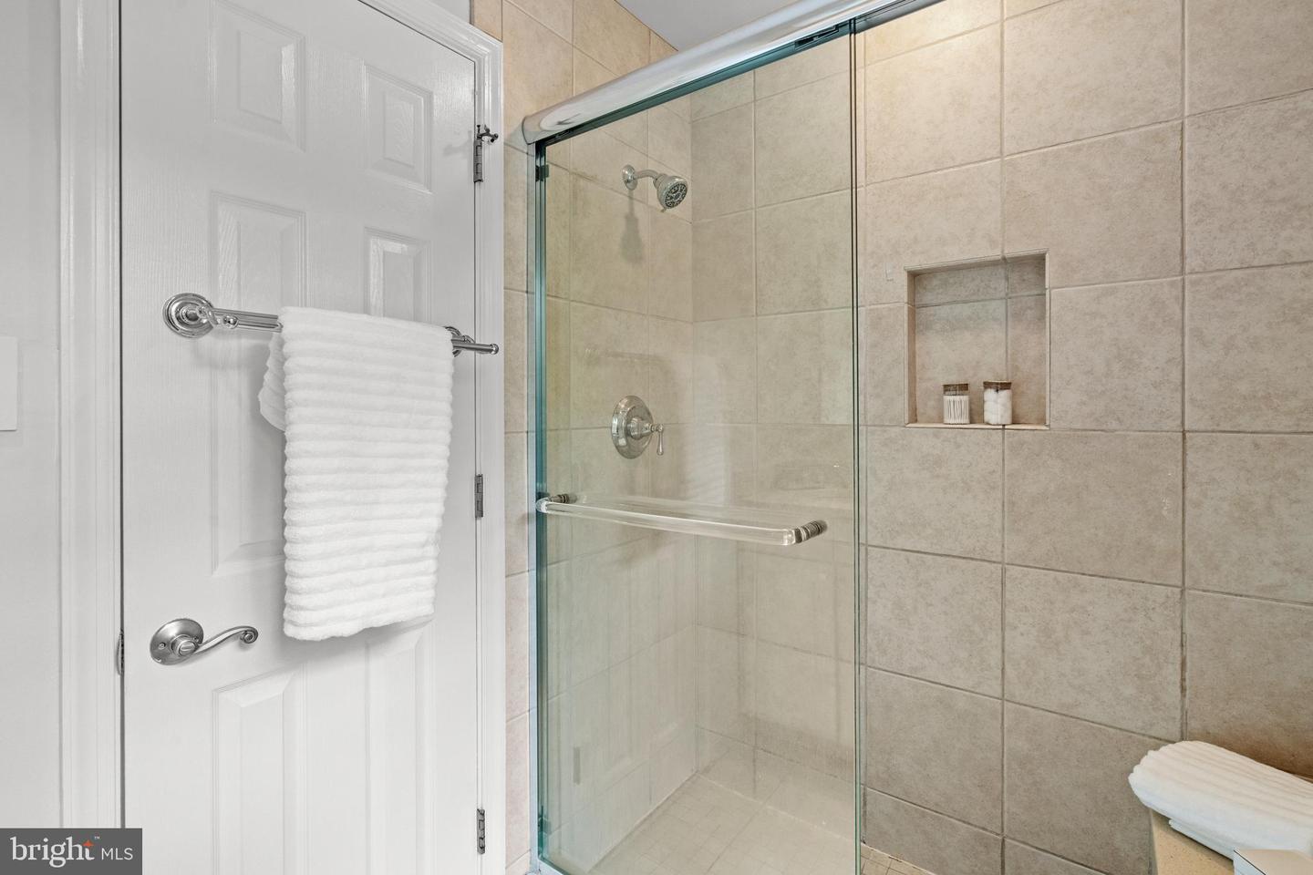Bathroom with a glass-enclosed tiled shower, recessed wall niche, and white towels.