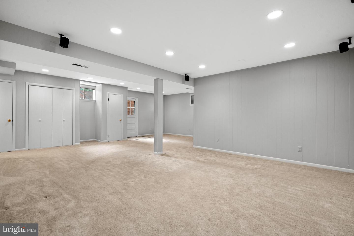 Empty carpeted basement with gray paneled walls, recessed lights, and a central support column.