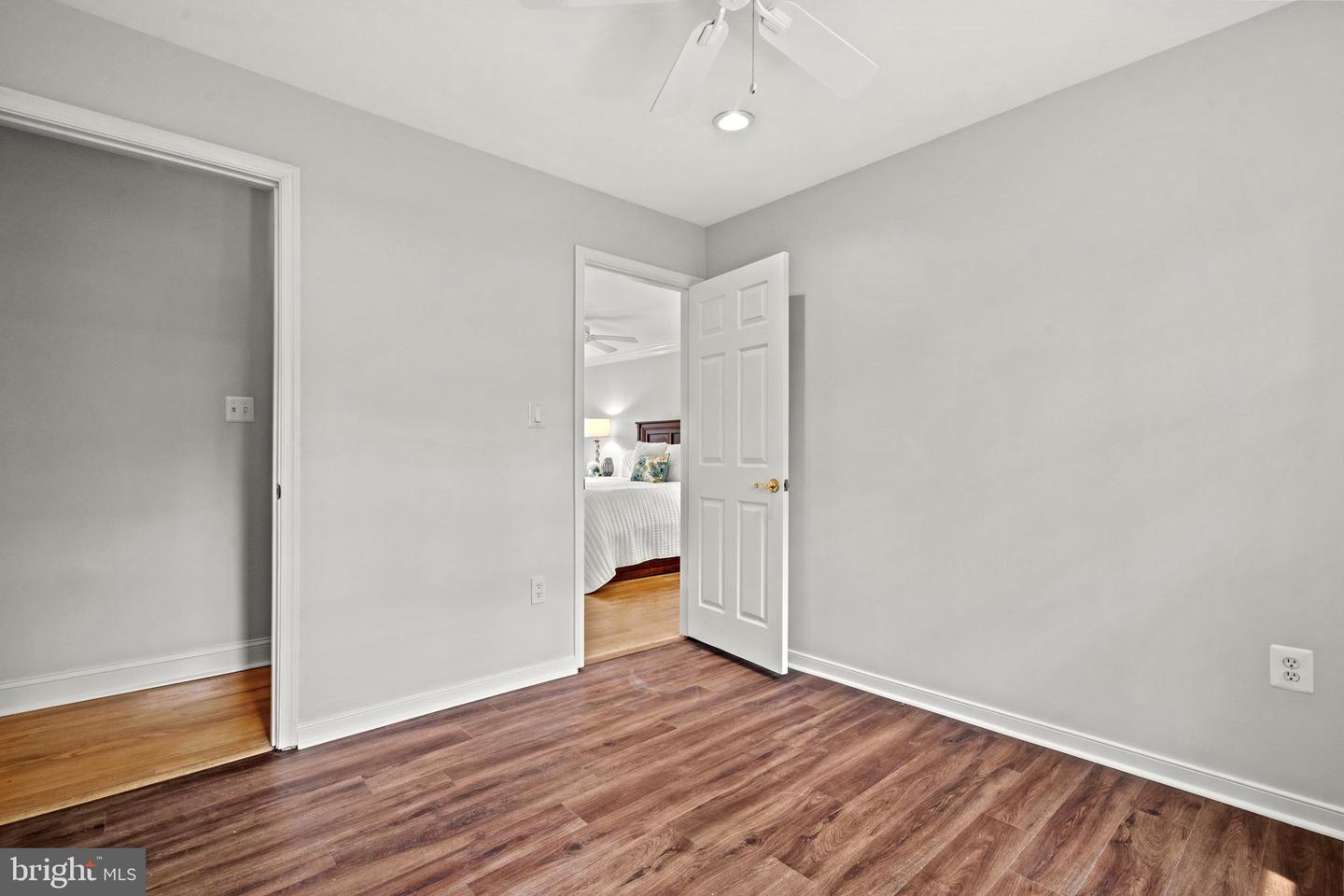 Empty bedroom with wood-look floors and an open doorway to a furnished bedroom.