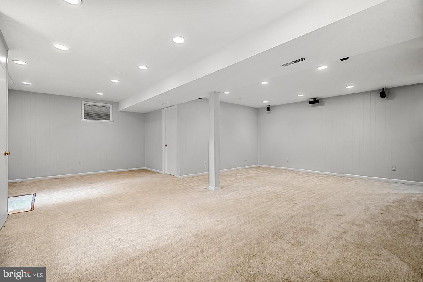 Empty basement recreation room with beige carpet, recessed lights, and a central support column.
