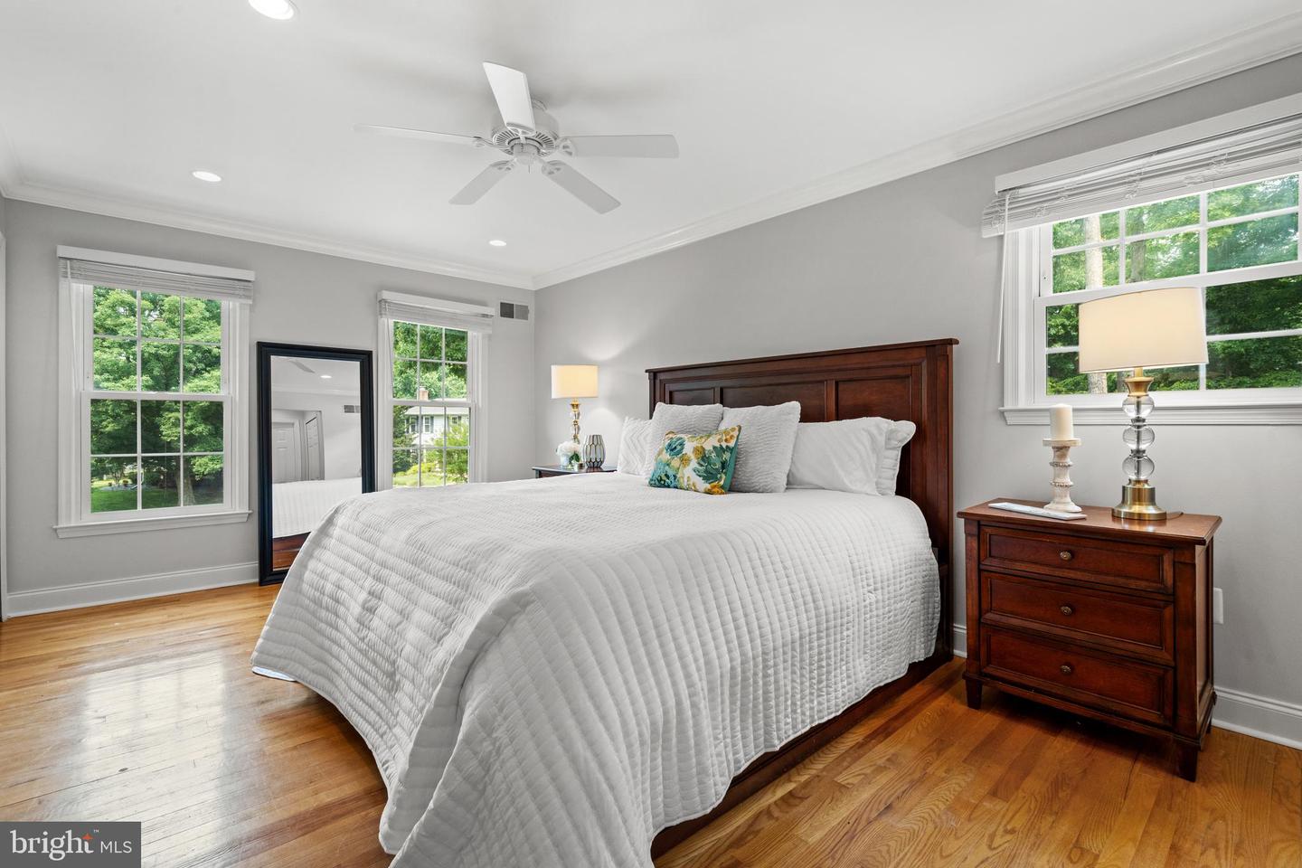 Bedroom with a large dark wood bed, white bedding, hardwood floors, and windows overlooking greenery.