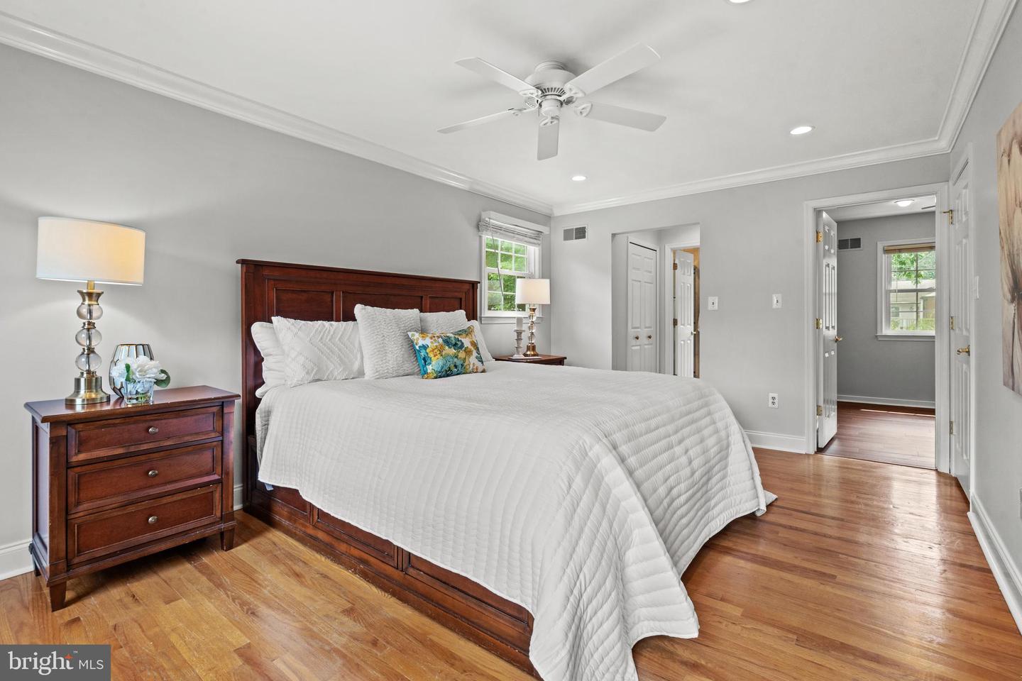 Bedroom with dark wood bed, white quilt, hardwood floors, and ceiling fan.