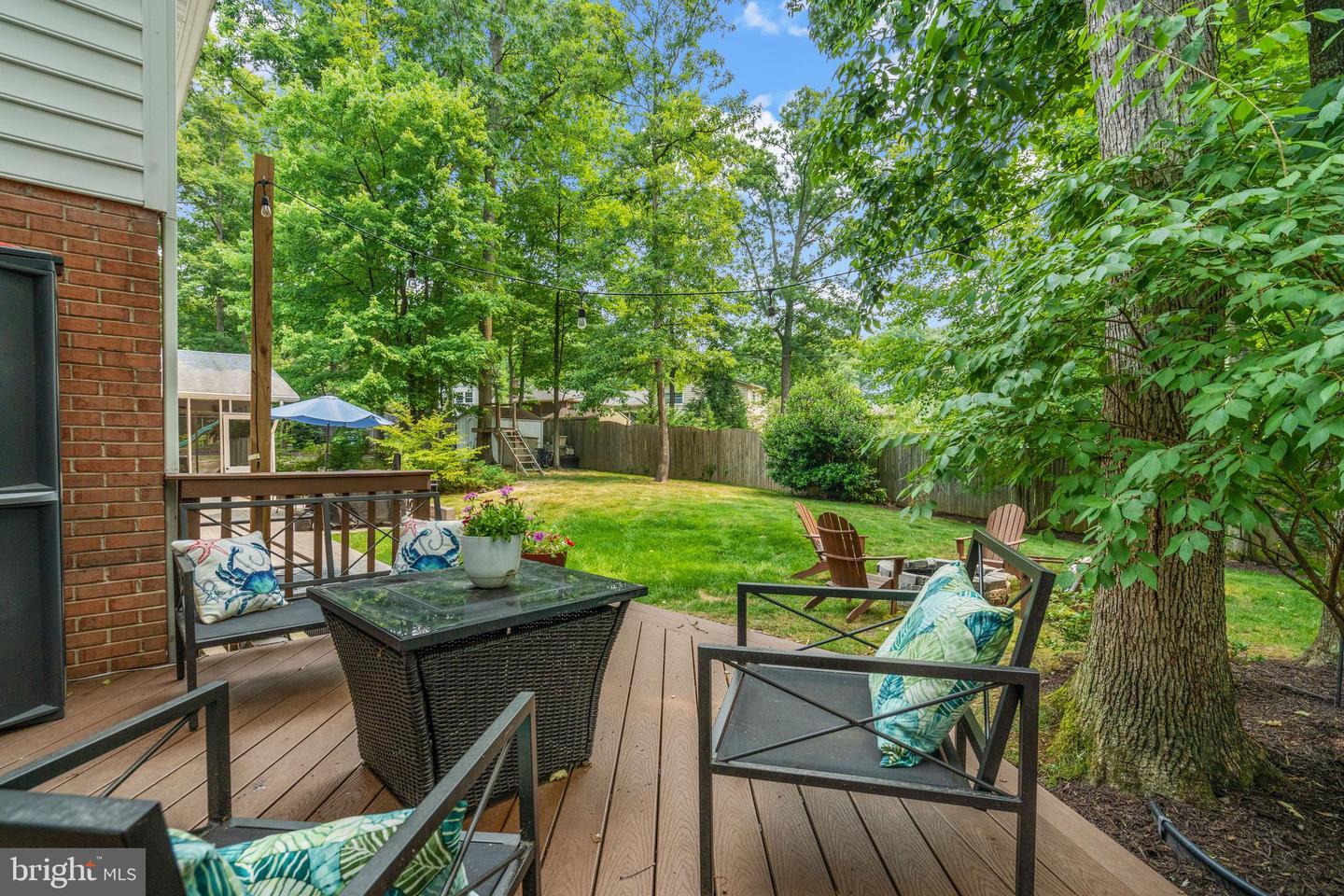 Furnished wood deck overlooking a fenced backyard lawn shaded by mature trees.