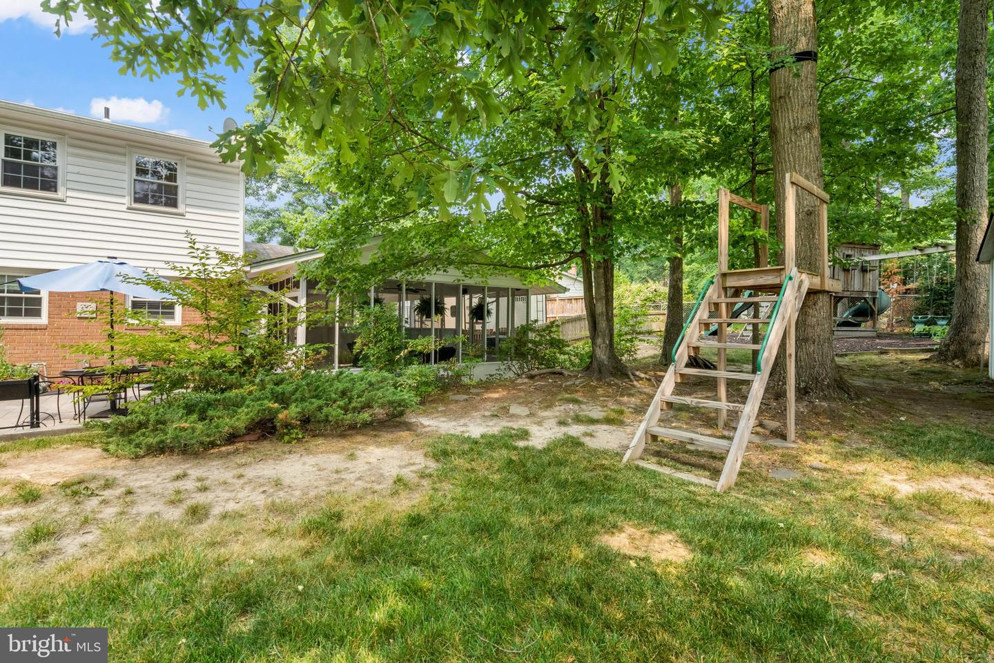 Backyard with a screened porch, patio seating, mature trees, and a wooden treehouse playset.