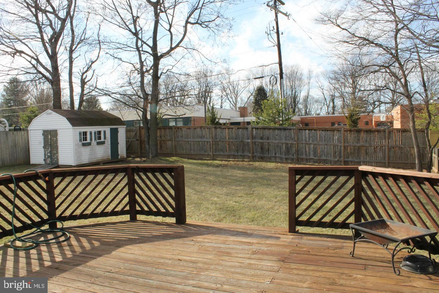 Fenced backyard with a wooden deck, white storage shed, and leafless trees.