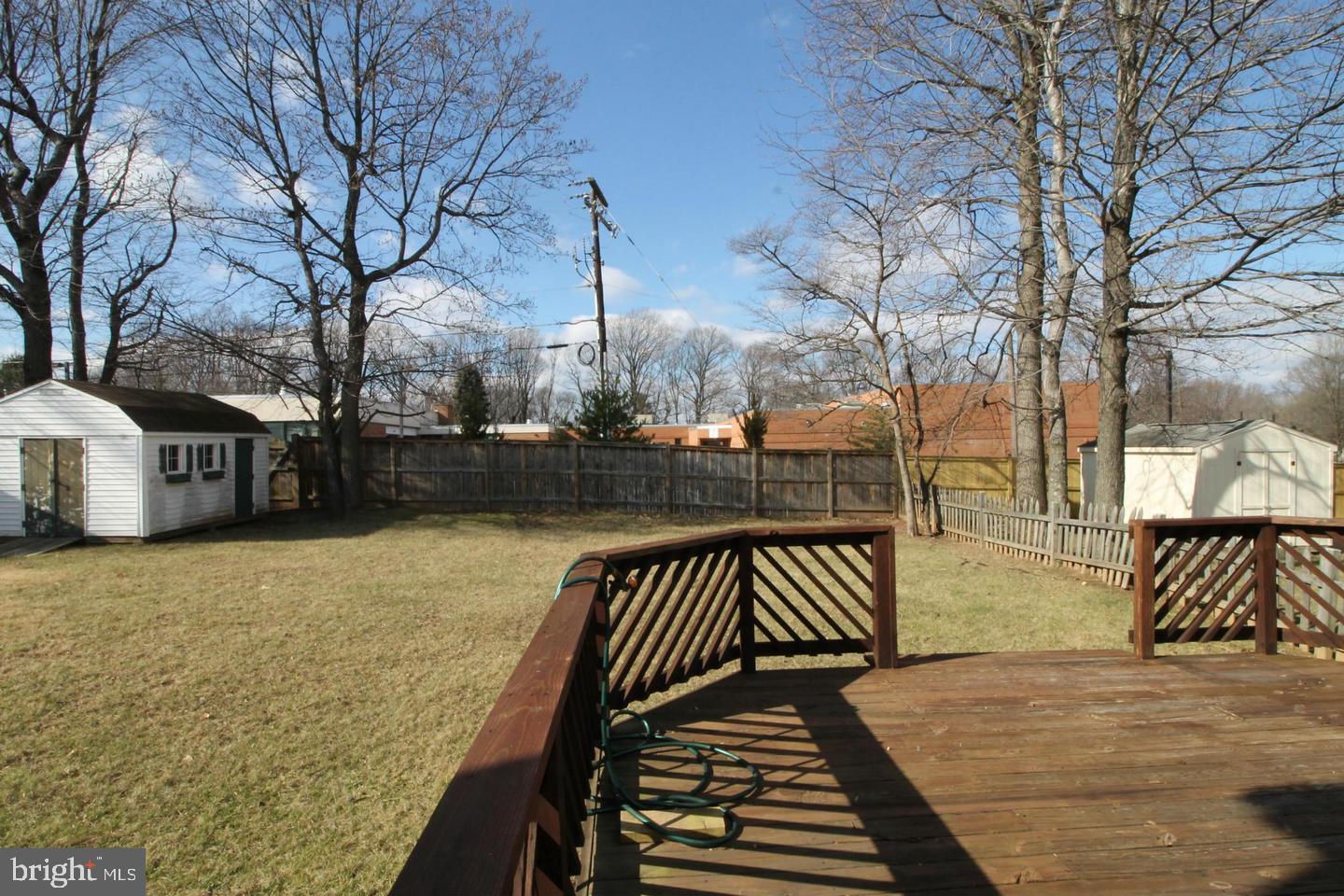 Fenced backyard with a wooden deck, two sheds, and leafless trees.