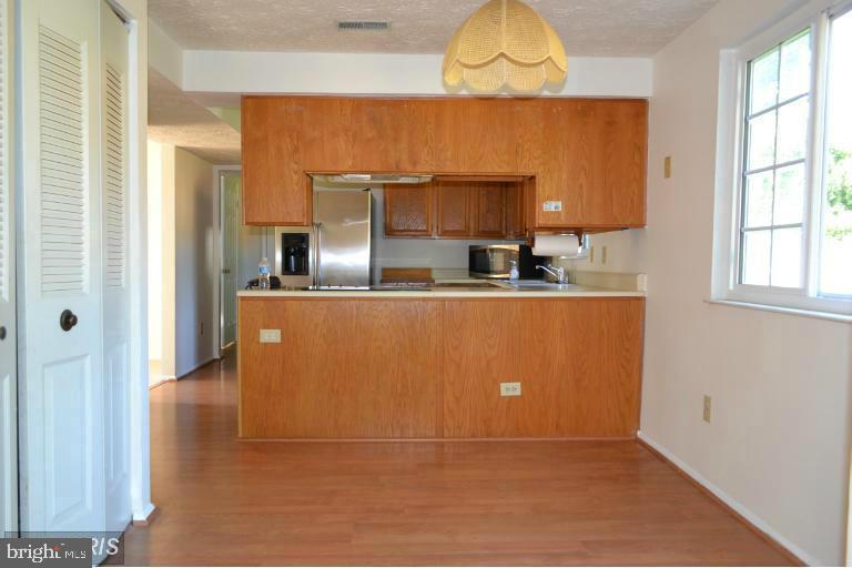 Kitchen with warm wood cabinets, a breakfast bar, stainless steel refrigerator, and wood-look flooring.