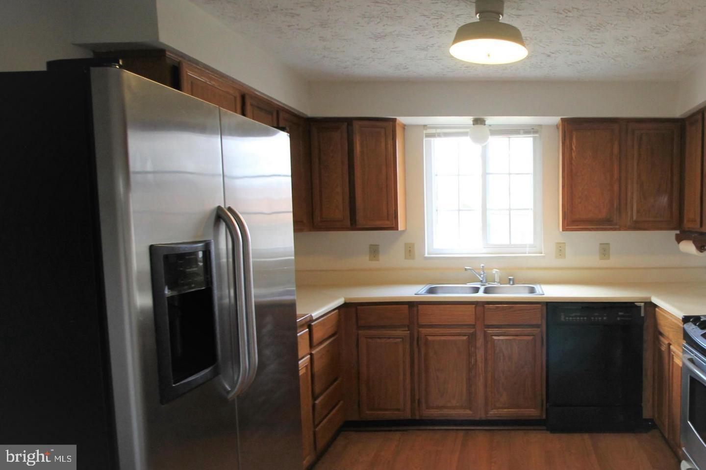 Kitchen with dark wood cabinetry, stainless steel refrigerator, and double sink beneath a window.