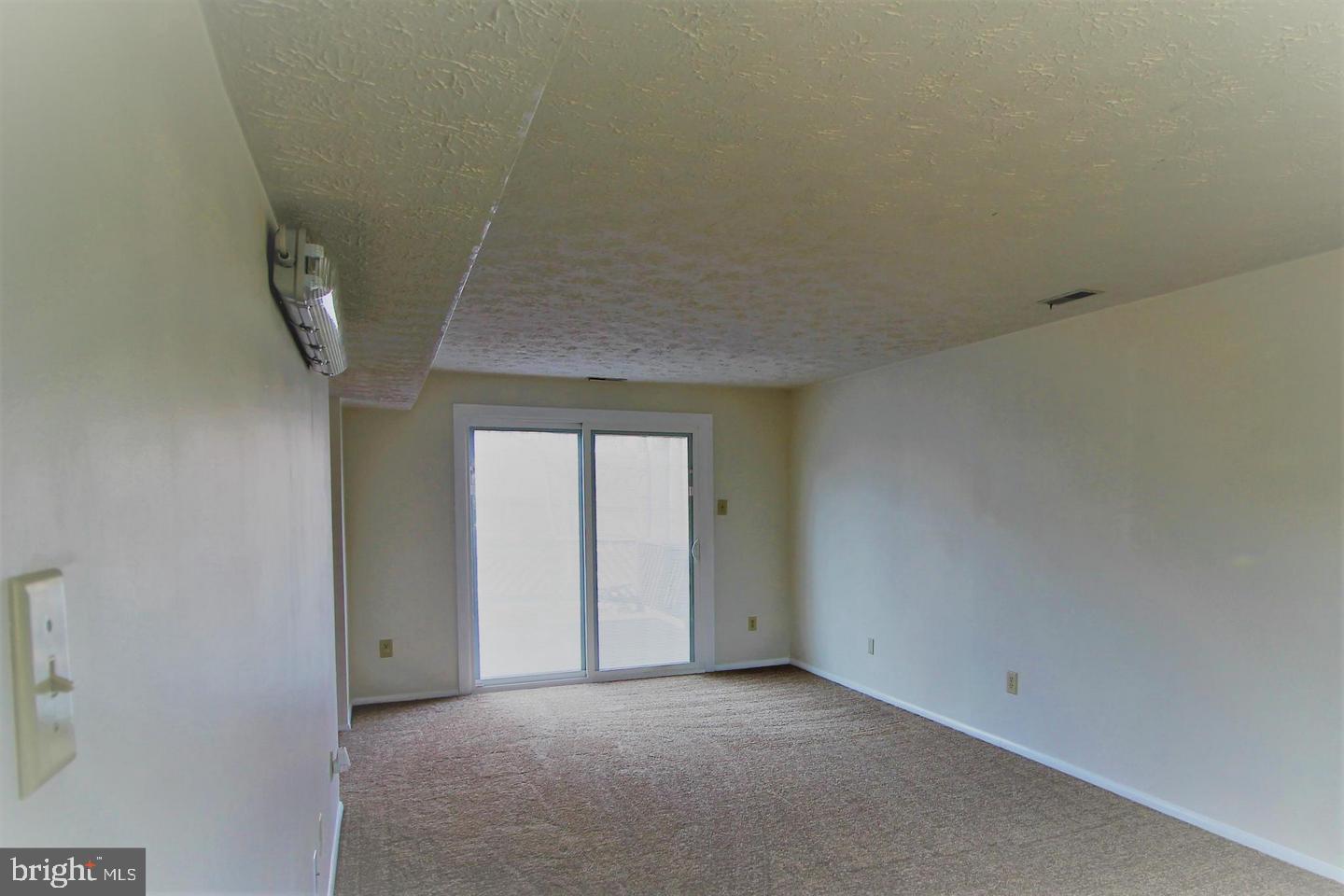 Empty carpeted room with sliding glass doors and a low textured ceiling.