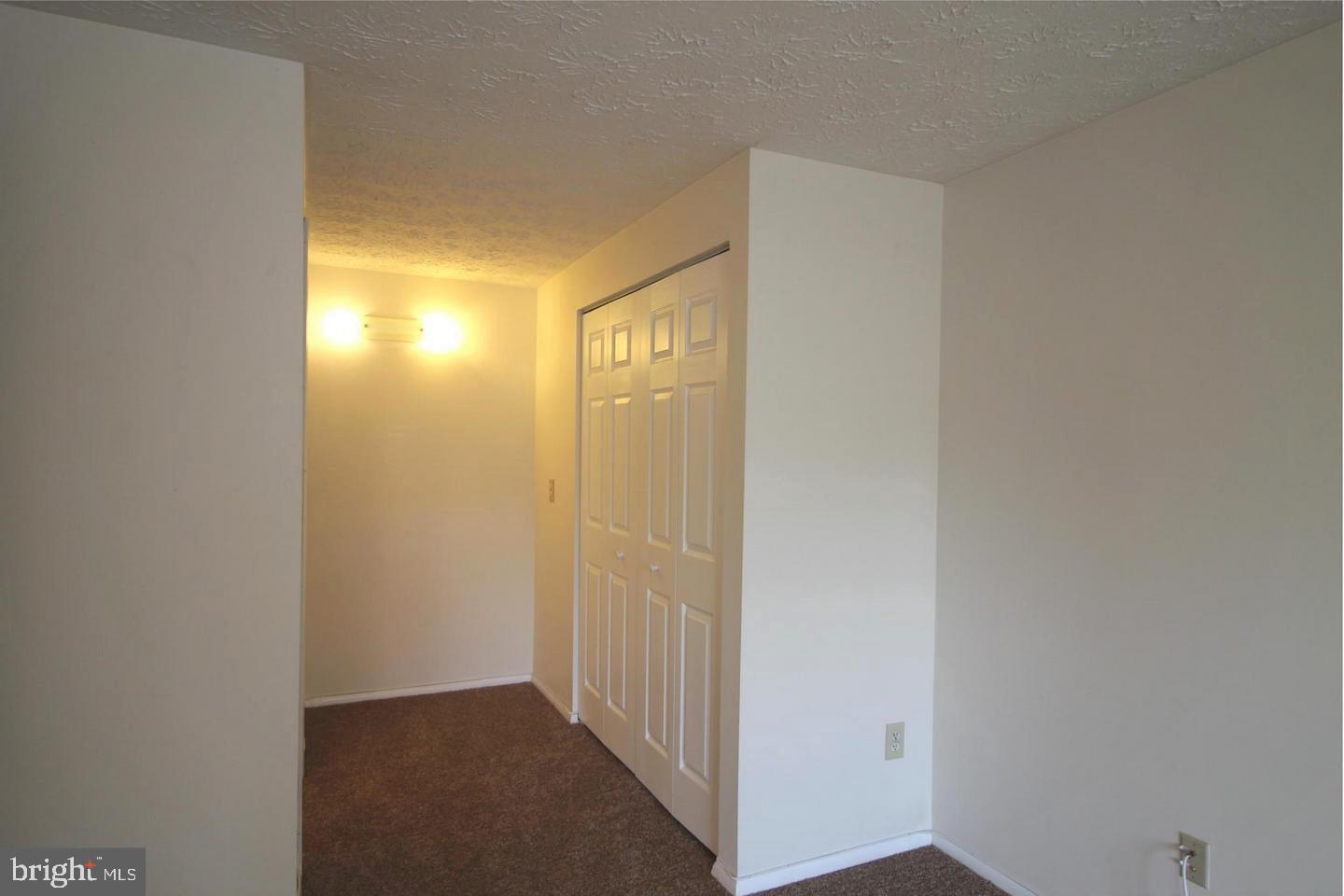 Carpeted hallway with paneled closet doors and a glowing wall fixture.