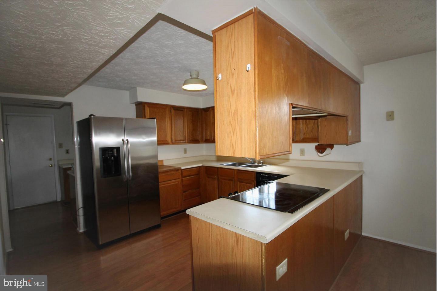 Kitchen with wood cabinetry, a cooktop peninsula, and stainless steel refrigerator.