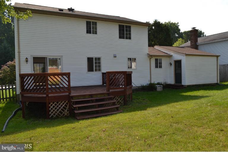 Rear of a two-story white-sided home with a raised wooden deck and broad lawn.