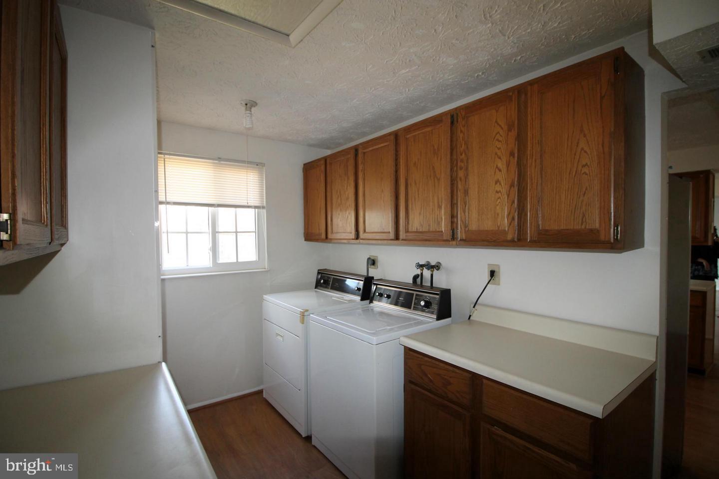 Laundry room with washer and dryer, wooden cabinets, and a long countertop.