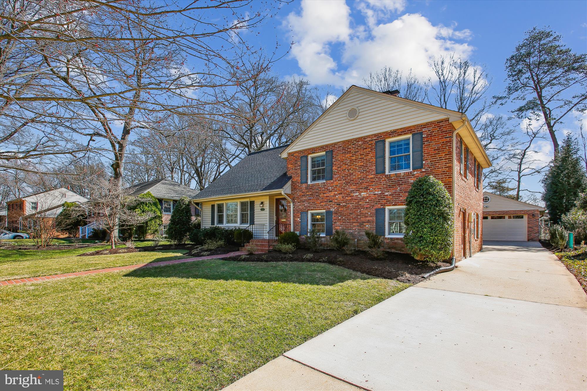 Two-story brick house with blue shutters, front lawn, and driveway to a detached garage.