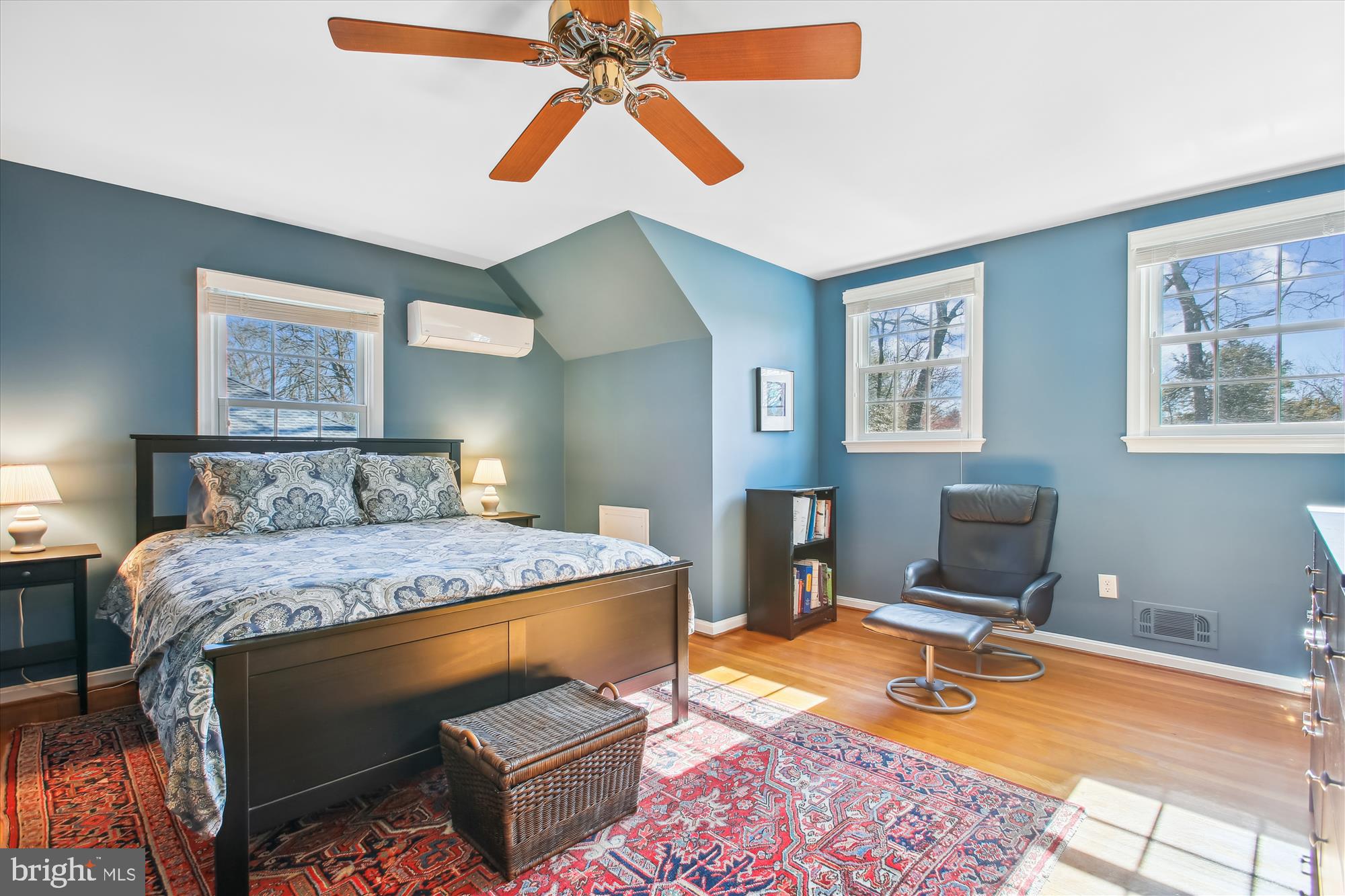 Furnished blue bedroom with patterned bedding, hardwood floors, and a black leather reading chair.