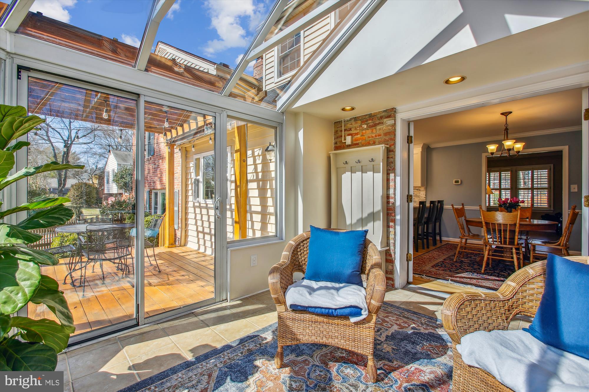 Sunroom with a glass ceiling, wicker chairs, and sliding doors opening onto a wooden deck.