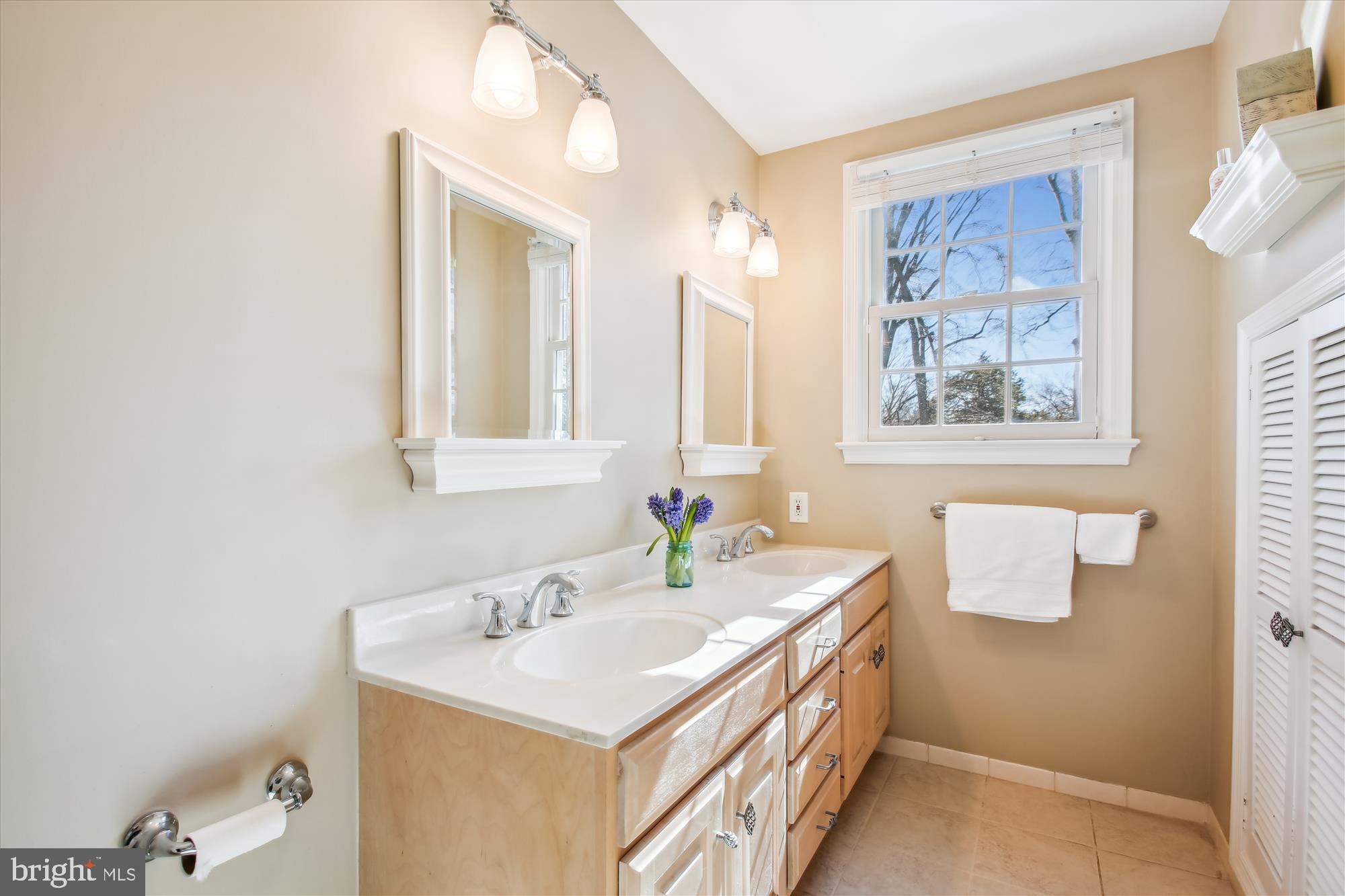 Bathroom with a double-sink vanity, light wood cabinets, and a large window.