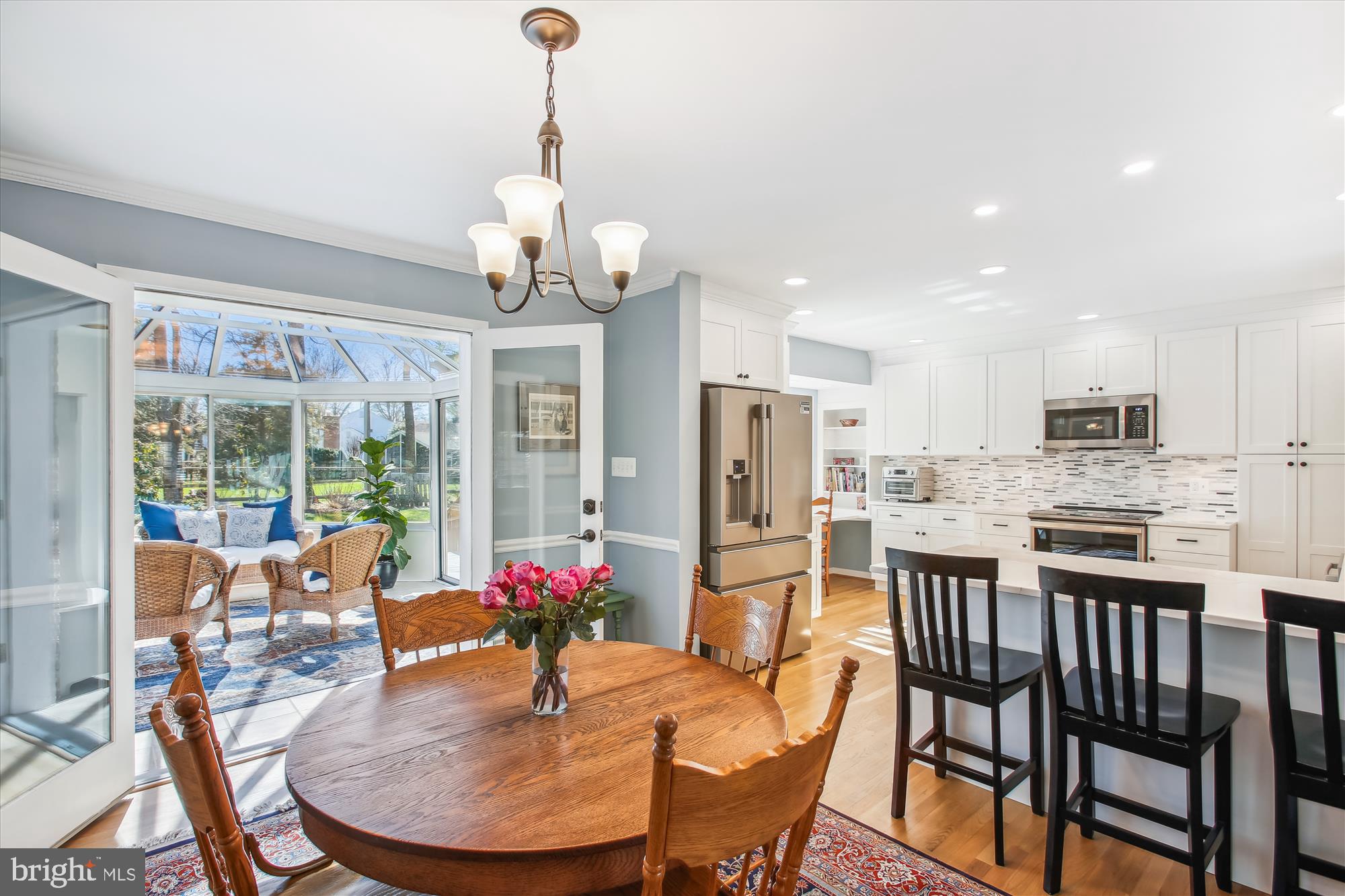 Kitchen and dining area with white cabinets, a round wooden table, and adjoining sunroom.