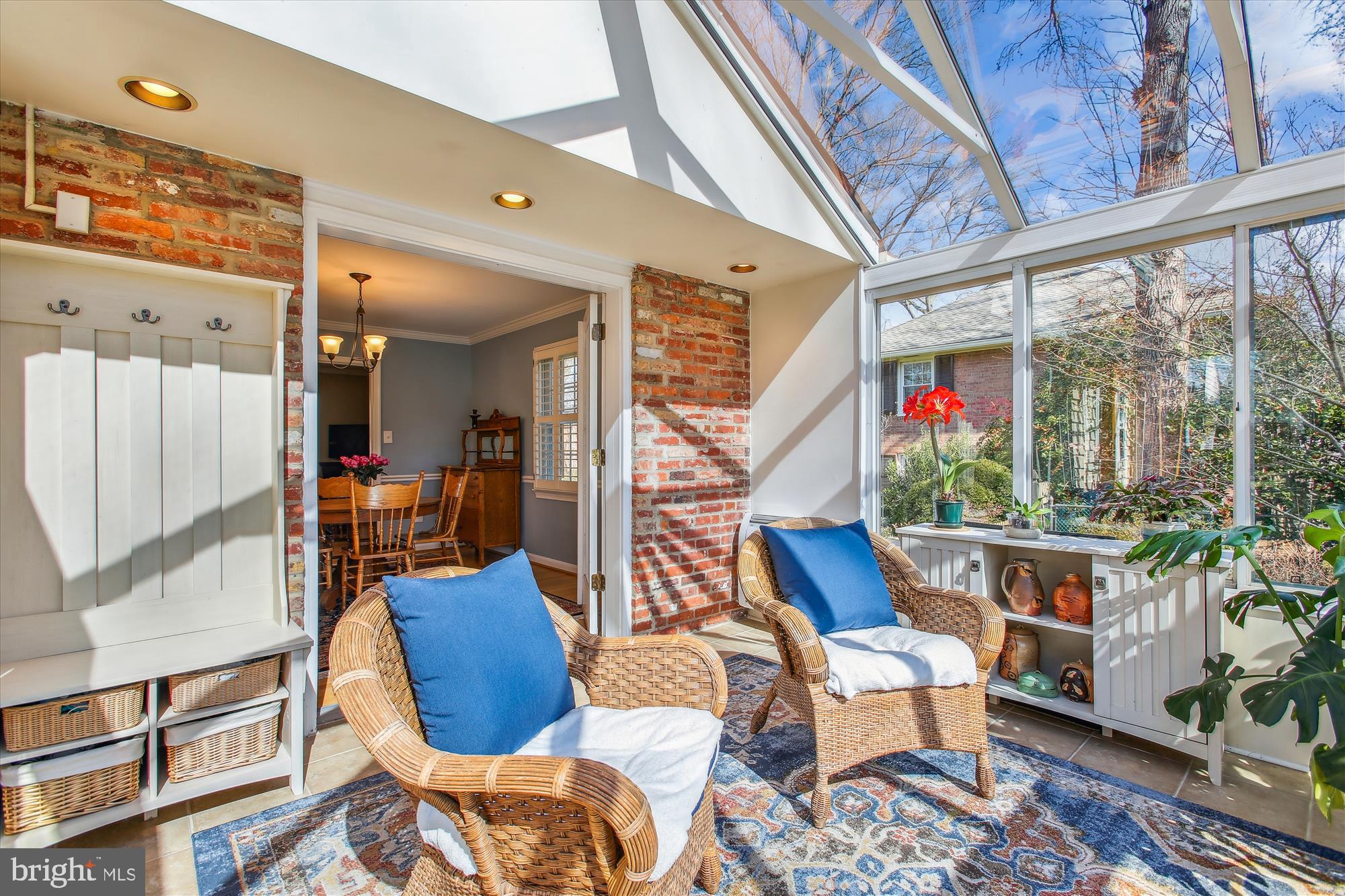 Sunroom with a glass ceiling, garden-view windows, exposed brick, and wicker chairs with blue cushions.