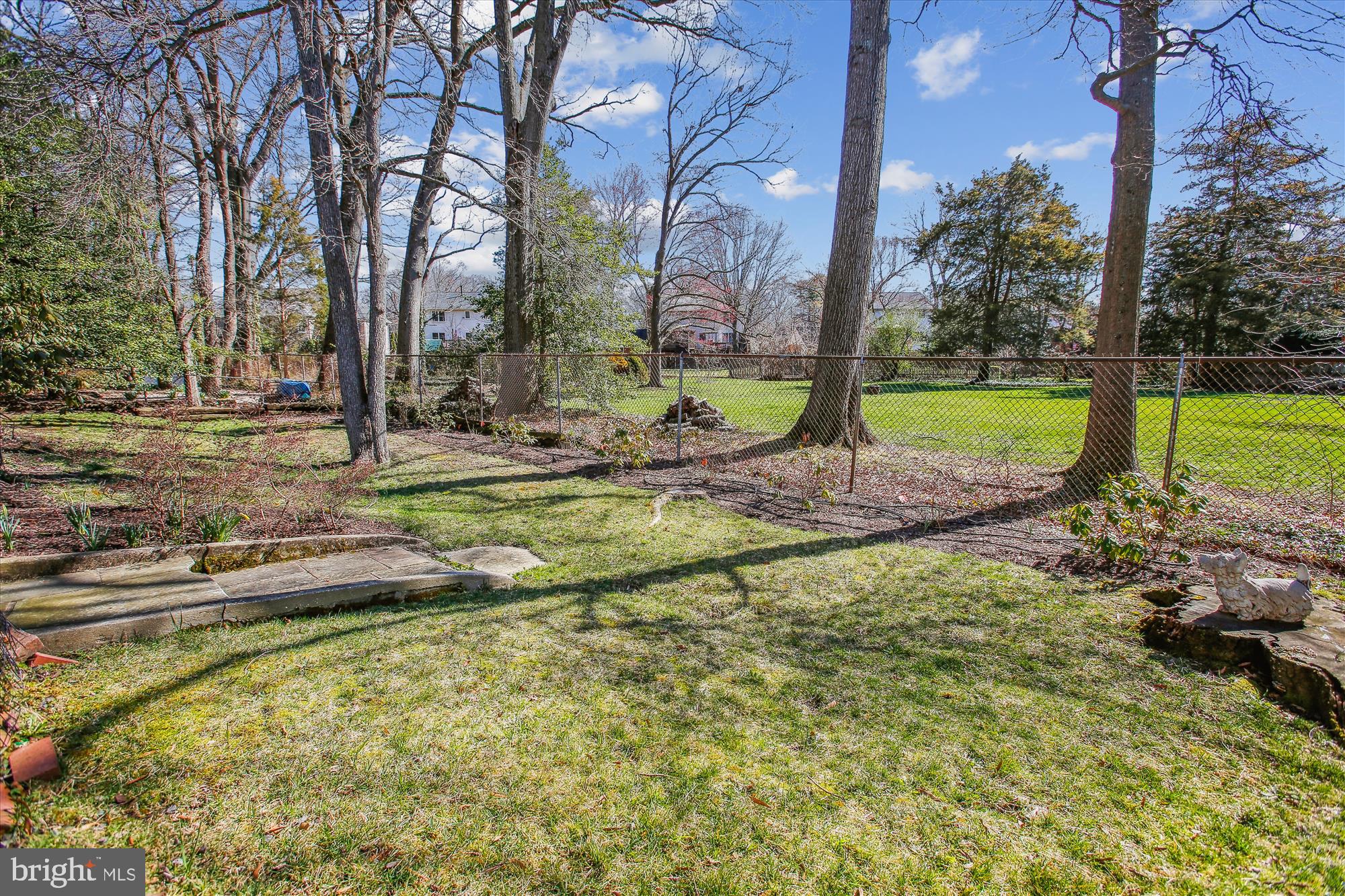 Grassy backyard with mature trees, garden beds, and a chain-link fence along the rear lawn.