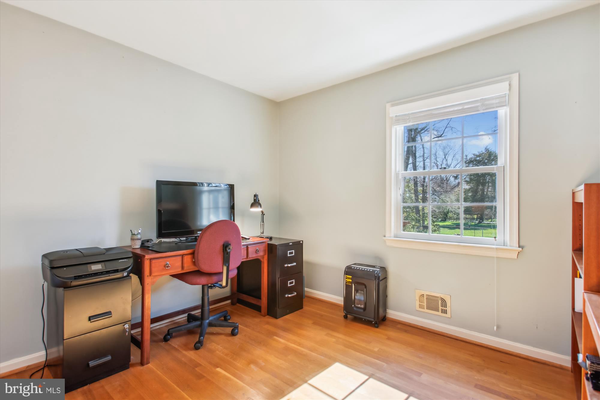 Home office with a wooden desk and red chair beside a large window overlooking the yard.
