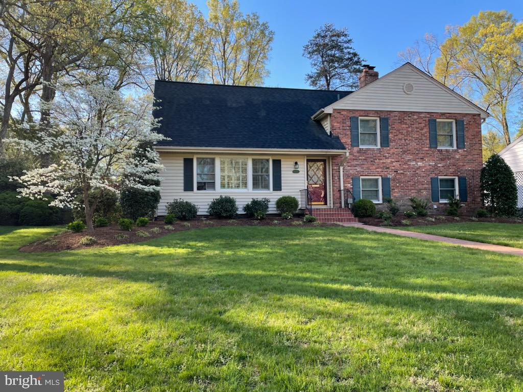 Two-story brick and white-sided home with a flowering tree, landscaped lawn, and walkway.