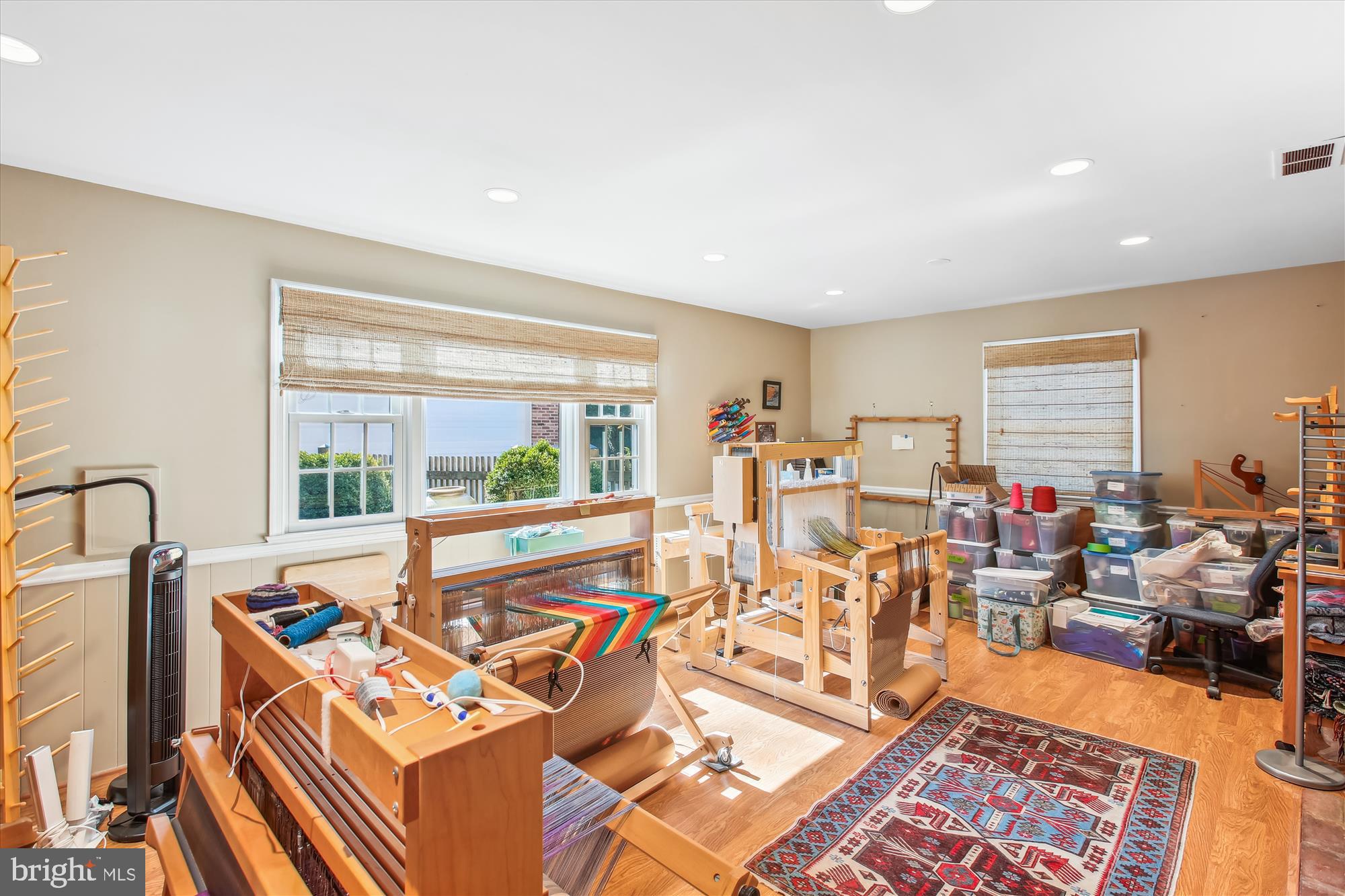 Craft room with wooden weaving looms, colorful yarn, and storage bins beside large windows.
