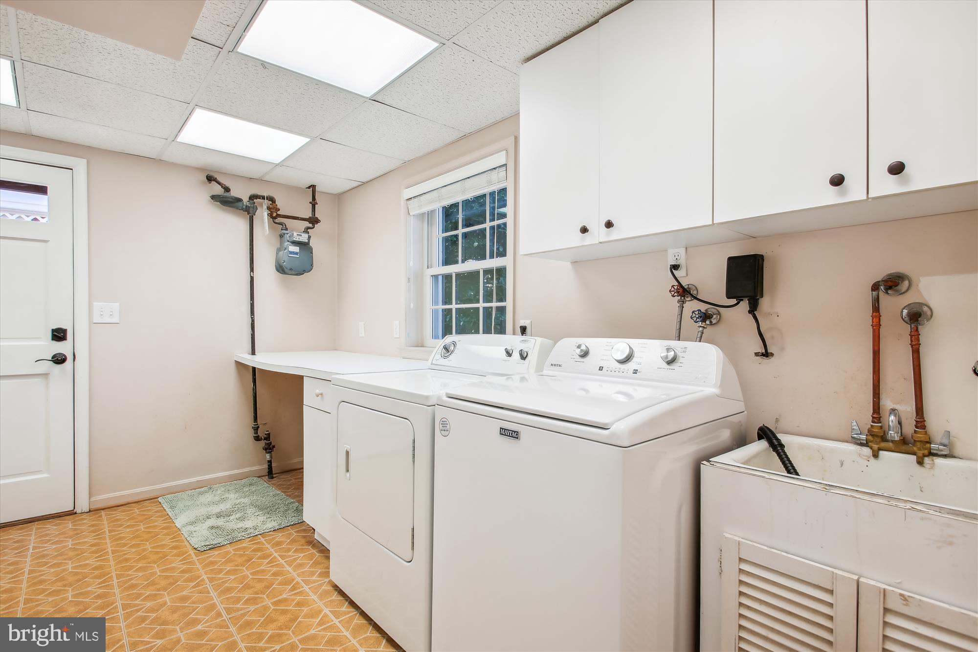 Laundry room with a washer and dryer, utility sink, and white upper cabinets.