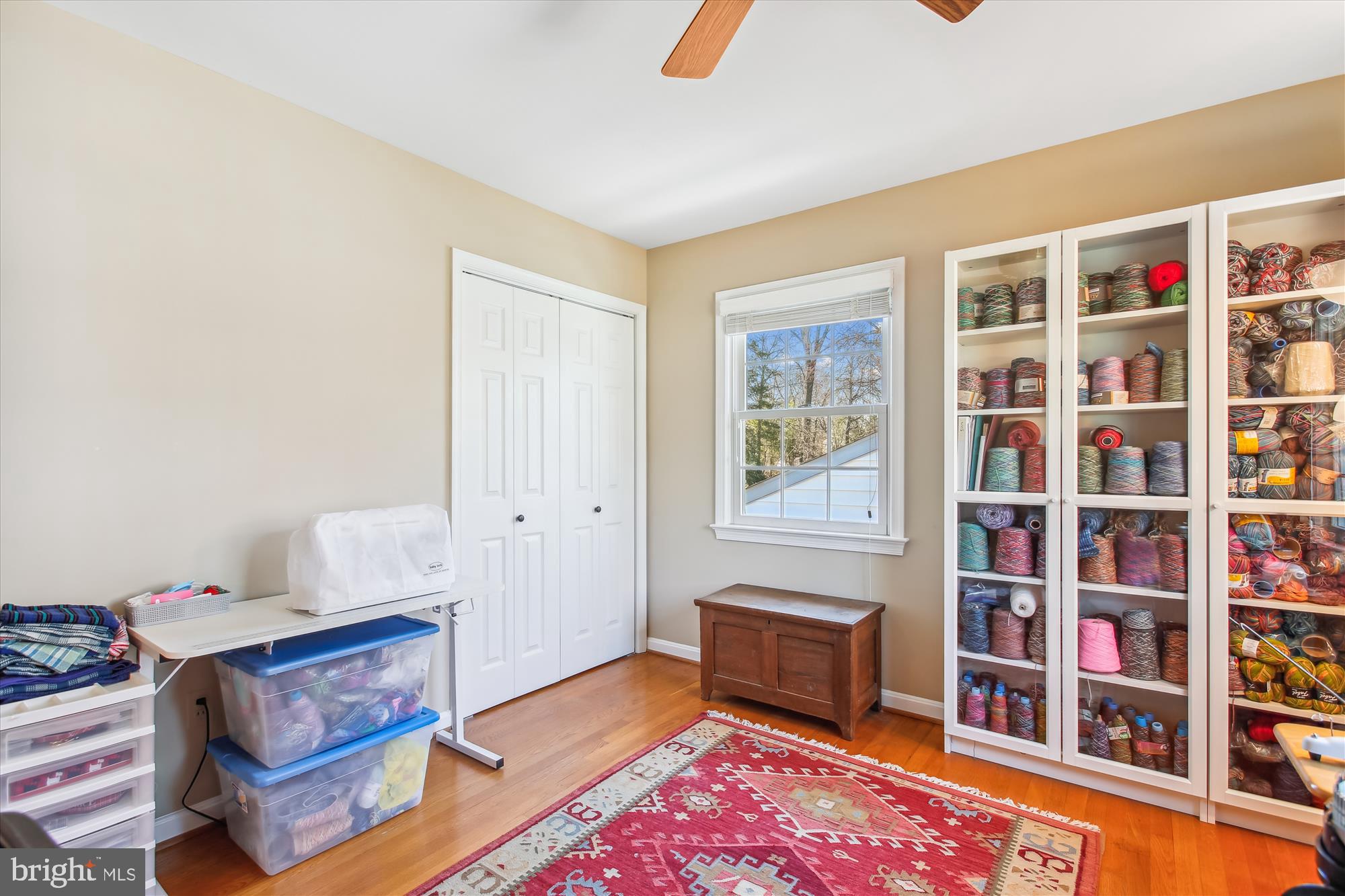 Craft room with yarn-filled cabinets, a sewing table, storage bins, and a red patterned rug.