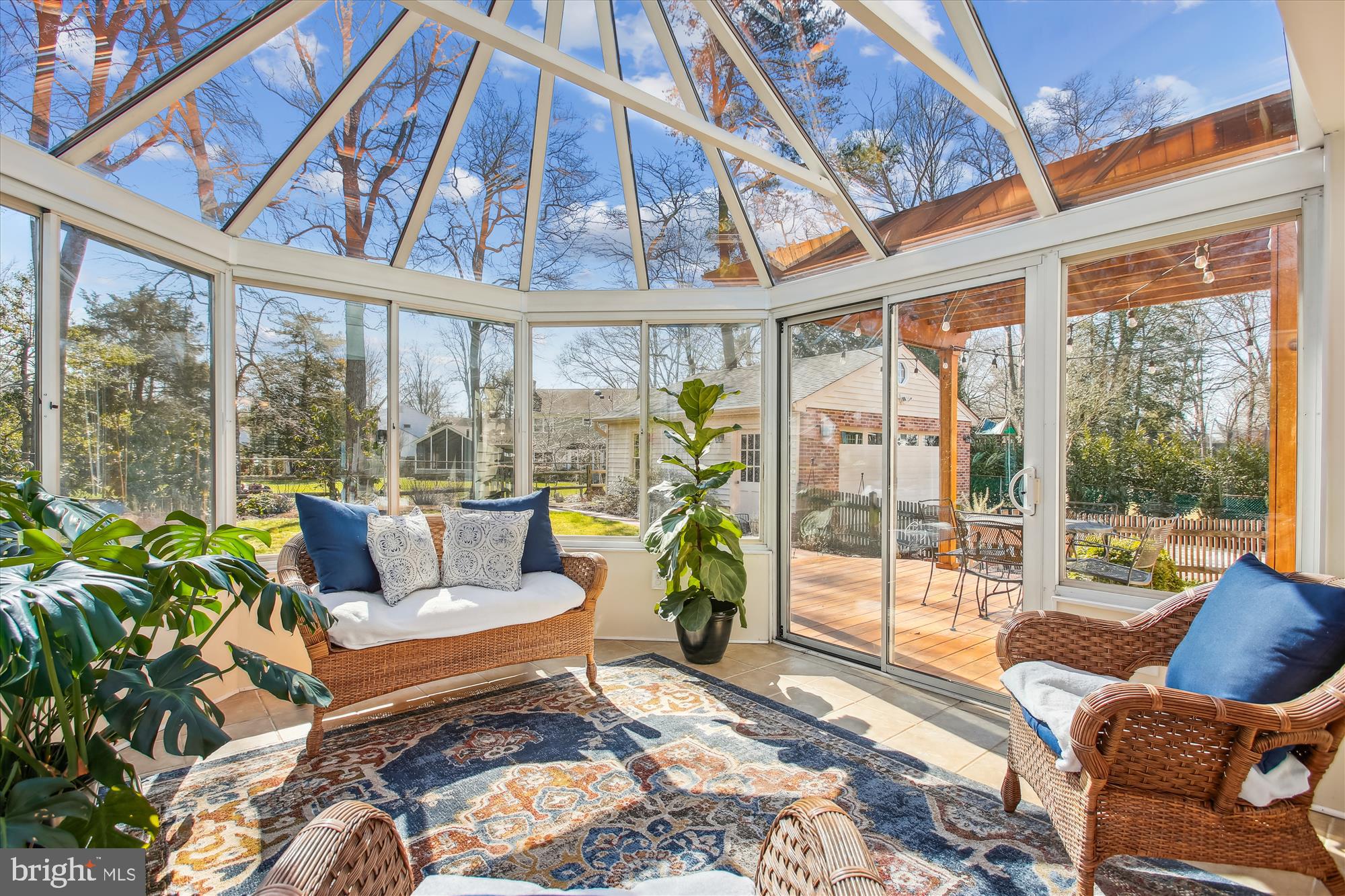 Furnished sunroom with a glass ceiling, wicker seating, and sliding doors to a wooden deck.