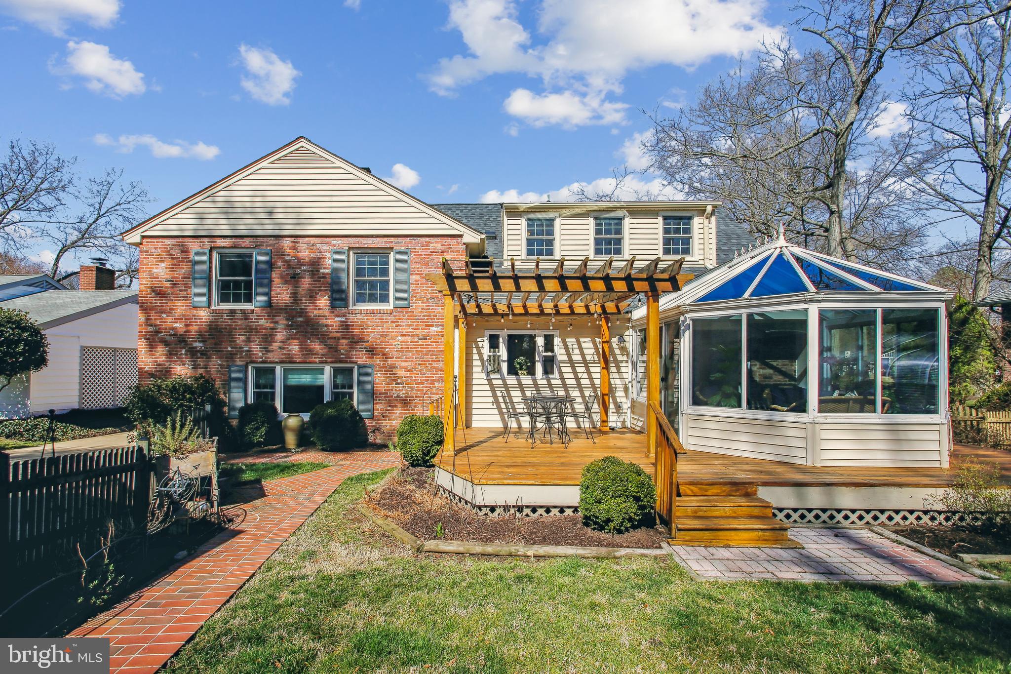 Rear of a brick-and-siding home with a pergola-covered deck and glass sunroom.
