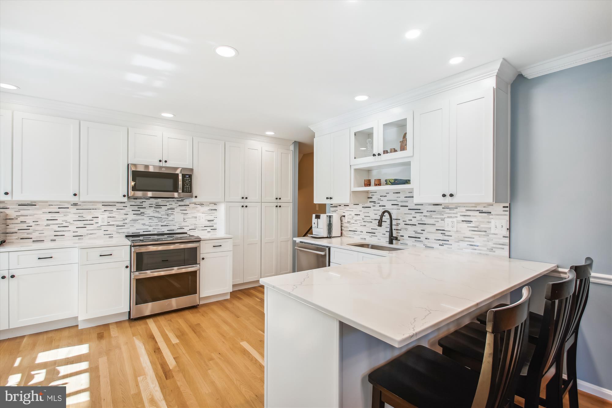 Bright kitchen with white cabinetry, stainless appliances, and a large island with dark bar stools.