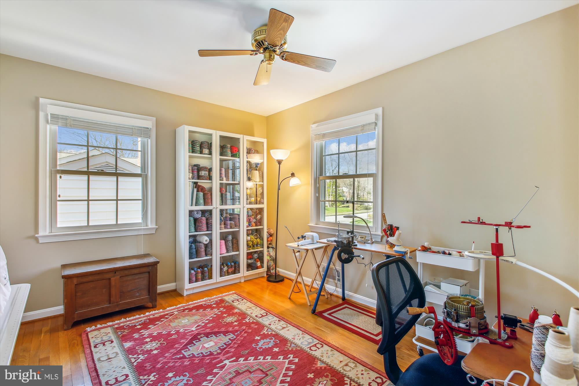 Sewing and craft room with yarn cabinets, worktables, and a red patterned rug.