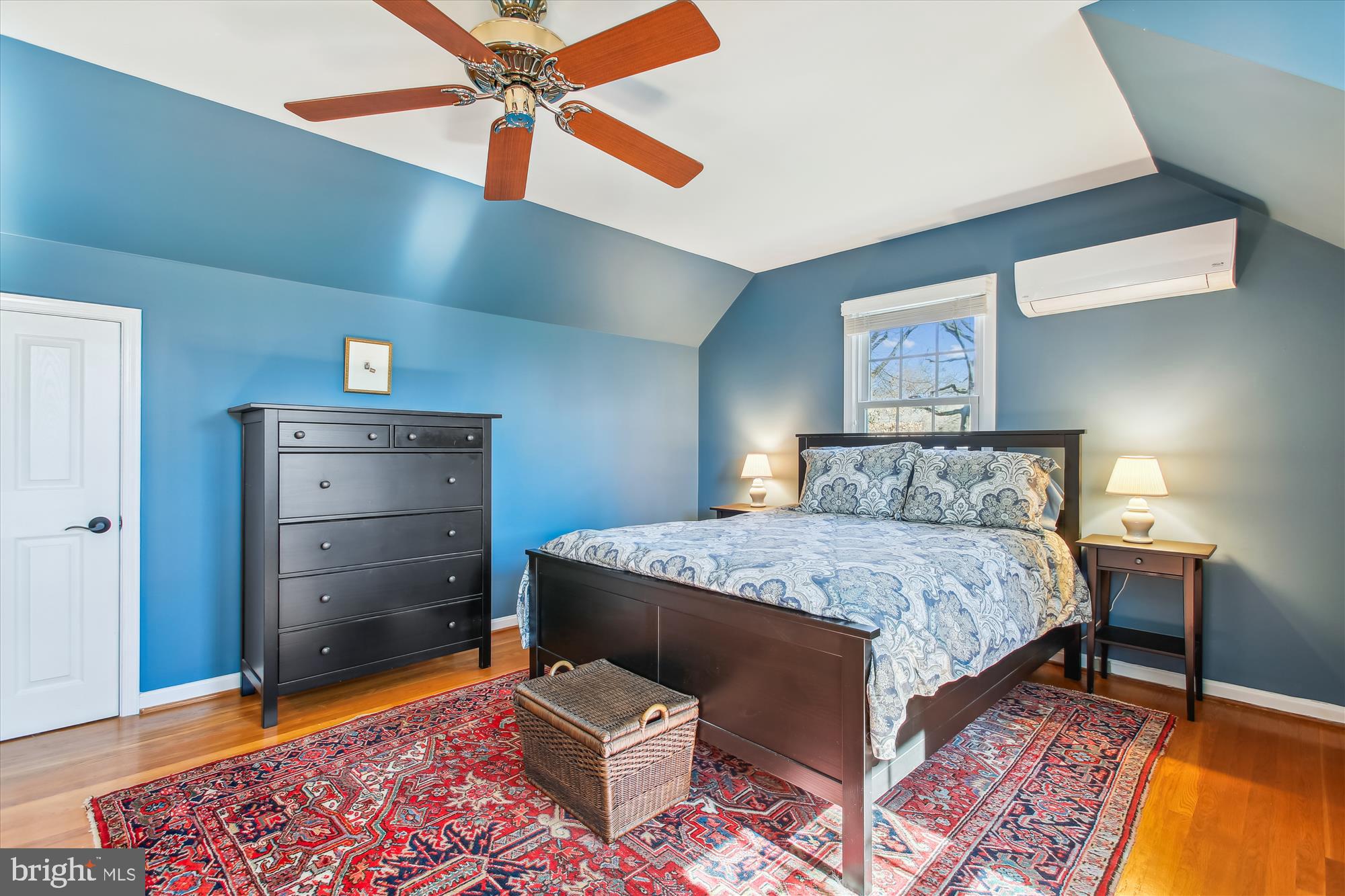 Furnished bedroom with blue walls, a vaulted ceiling, dark wood furniture, and a large patterned rug.